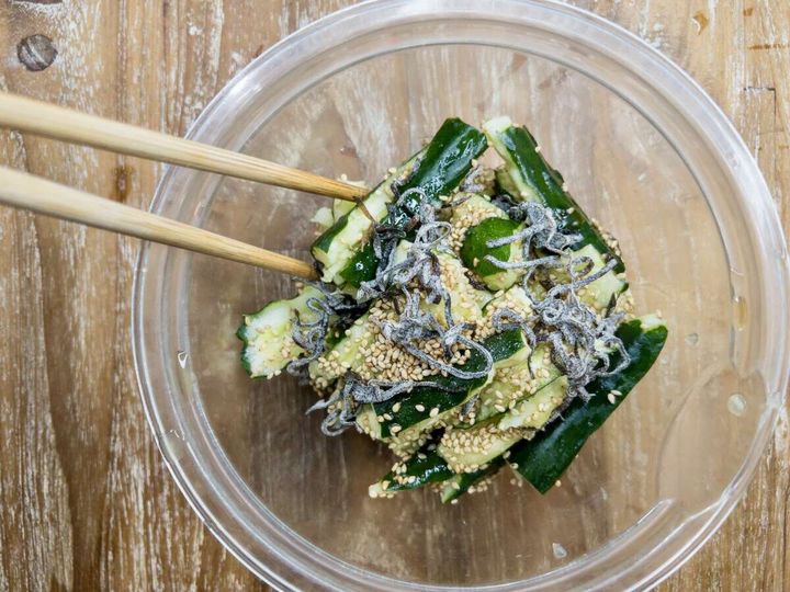 透明なボウルの中でちぎったきゅうりと塩昆布、ごまを箸で混ぜている俯瞰