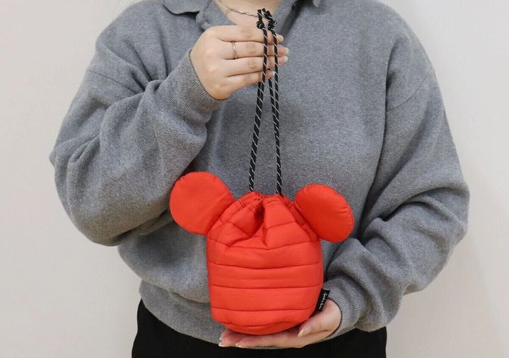 灰色の服を着た女性が赤いミッキーシェイプの巾着を手に持っている