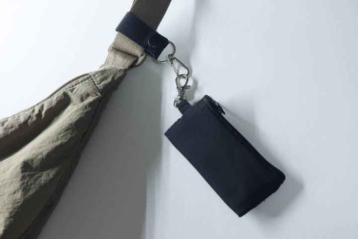 バッグのベルトに取り付けた小物ホルダーに黒いポーチを吊り下げている