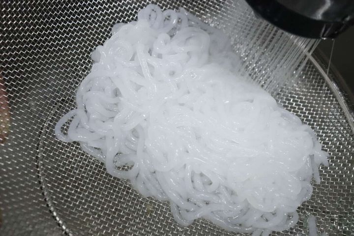 ザルに入ったこんにゃくヌードルを水で洗っている様子