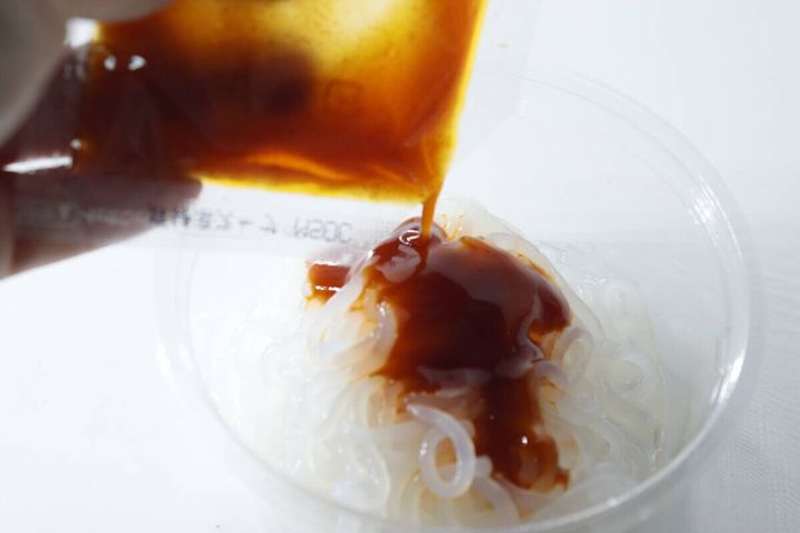 カップに入れたこんにゃくヌードルにスープを注ぐ手元