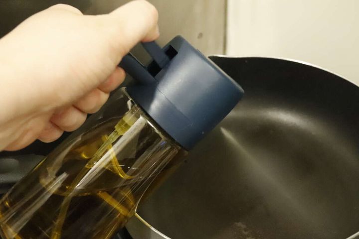 フライパンにオイルをスプレーしている手元