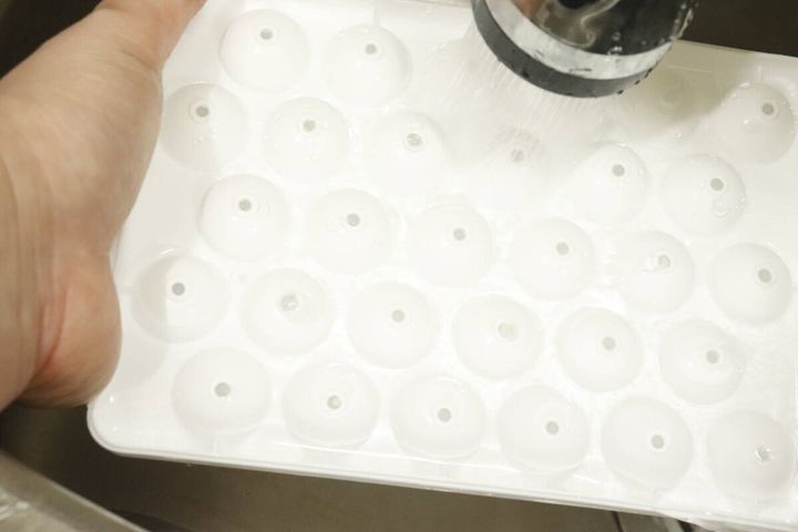 凍った製氷トレーに水をかけて氷を外しやすくしている様子