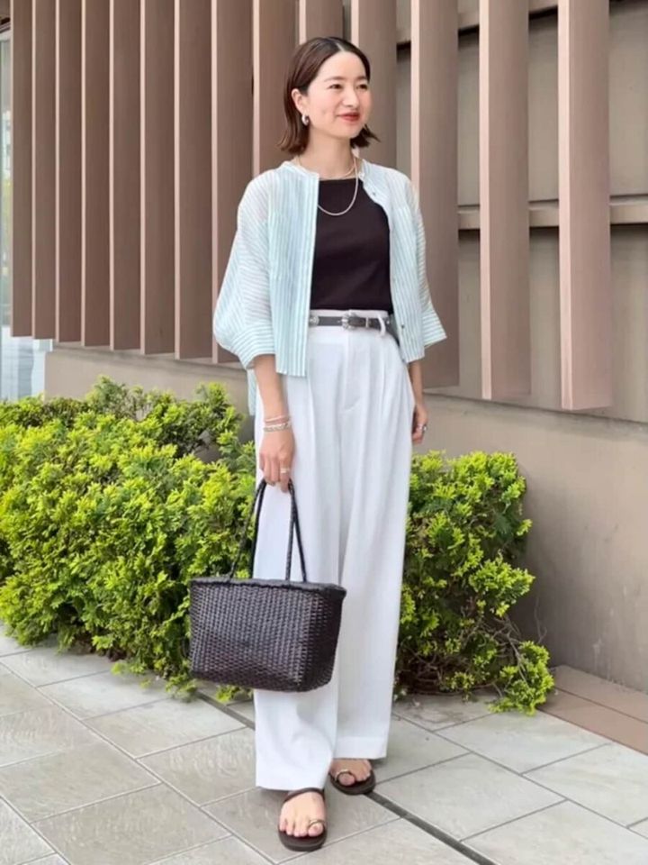 グリーンストライプのシアーシャツと白いワイドパンツを着用し、笑顔で立つ女性