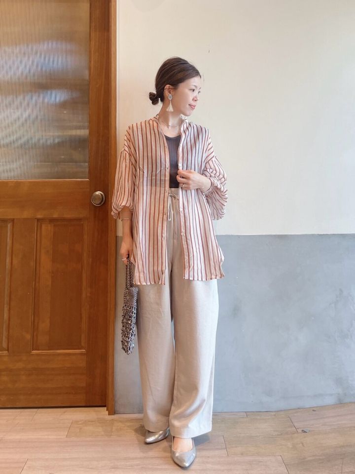 ストライプ柄シアーシャツとベージュのワイドパンツを着用し、バッグを持つ女性