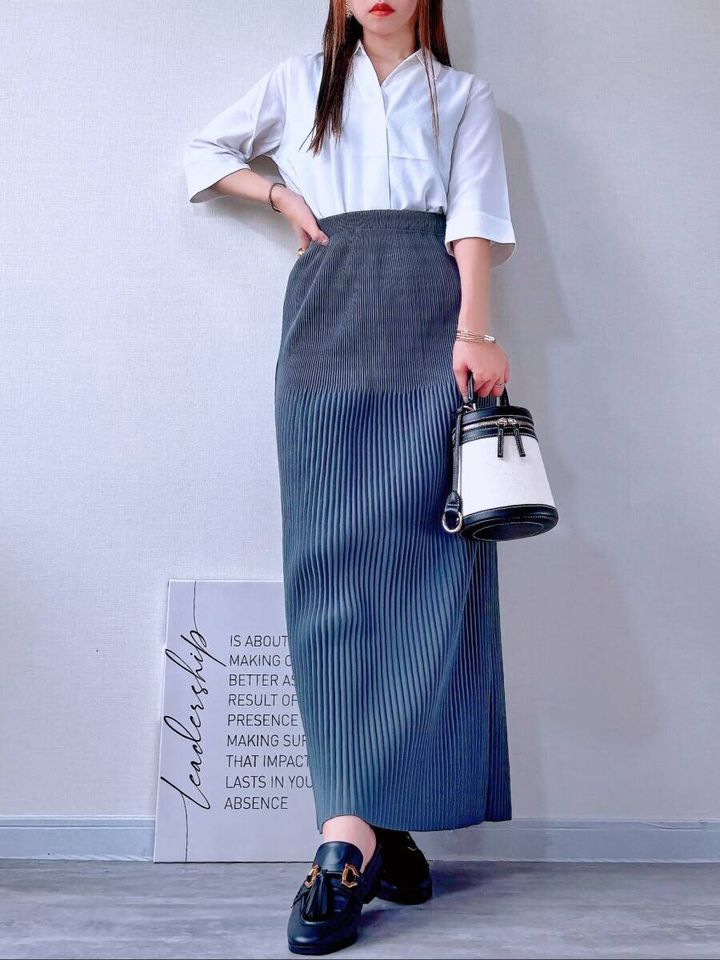 白いブラウスを前だけインし、グレーのプリーツスカートを合わせた女性の全身