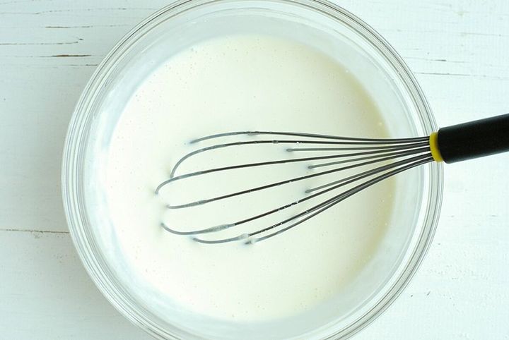 透明なボウルに入った牛乳やヨーグルトが混ざった生地を泡立て器で混ぜている様子