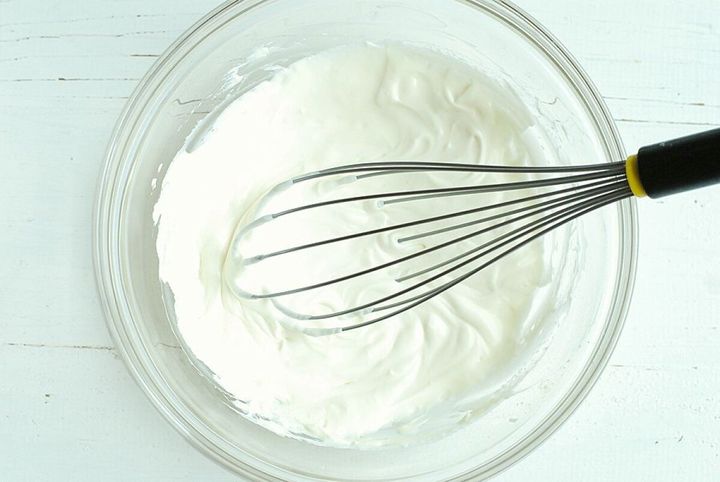 透明なボウルに入ったクリームチーズを泡立て器で混ぜている様子
