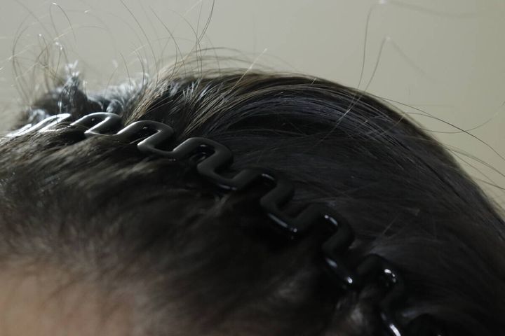 女性の髪に装着された黒いウェーブ状のカチューシャ。髪をしっかりホールドしている。