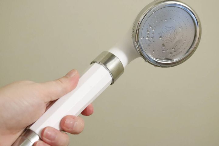 手で持ったシャワーヘッドに水滴が付いている様子