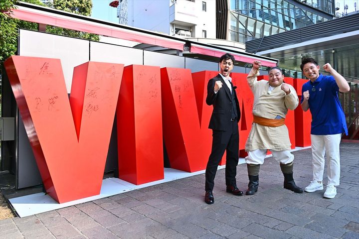 東京・赤坂サカス広場の『VIVANT』モニュメント前で「ドラム、アメリカへ行く！」出発式を行った（左から）都留拓也（ラパルフェ）、ドラム、MLBオールスター盛り上げ隊長・杉谷拳士 （C）TBS width=
