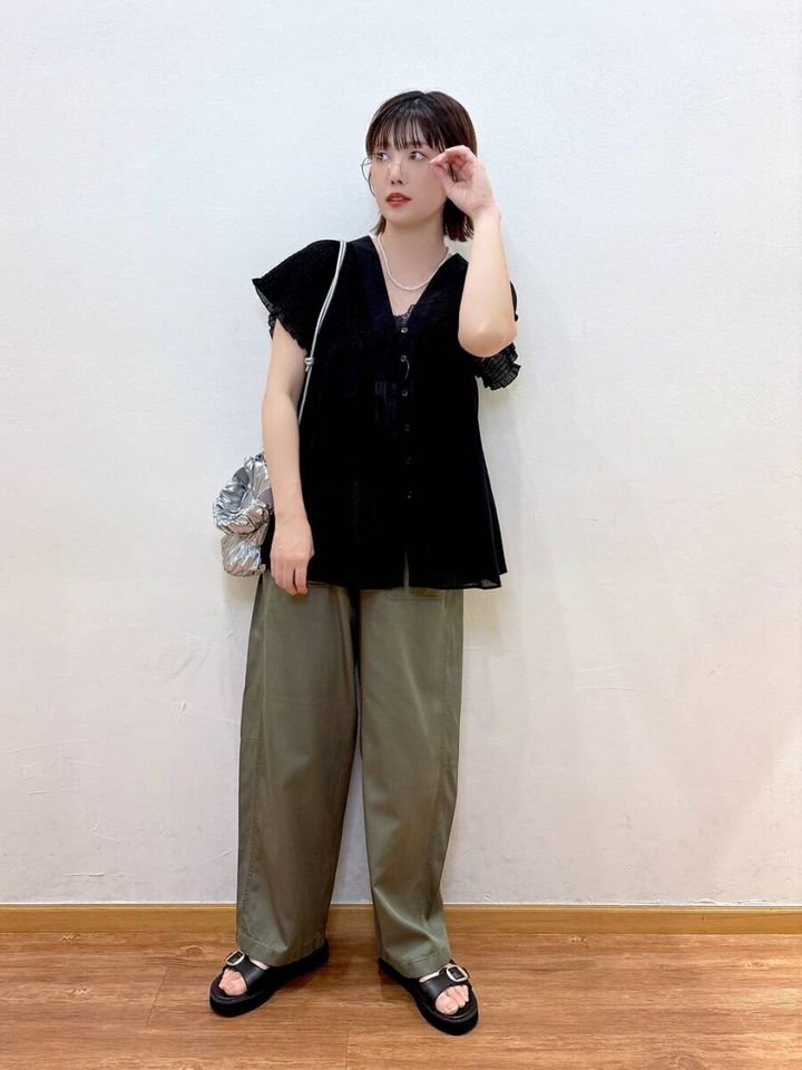 黒のギャザーブラウスとカーキワイドパンツを着てメガネに手を添える女性