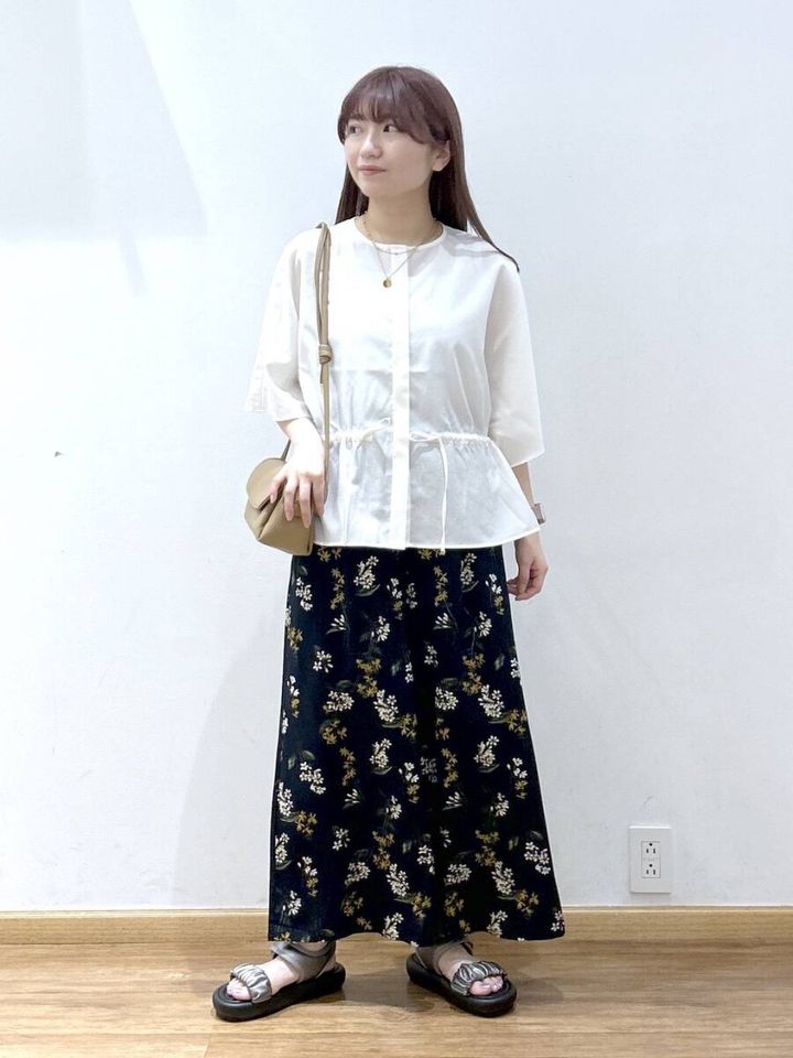 白のドローストリングブラウスと花柄ロングスカートを着た女性