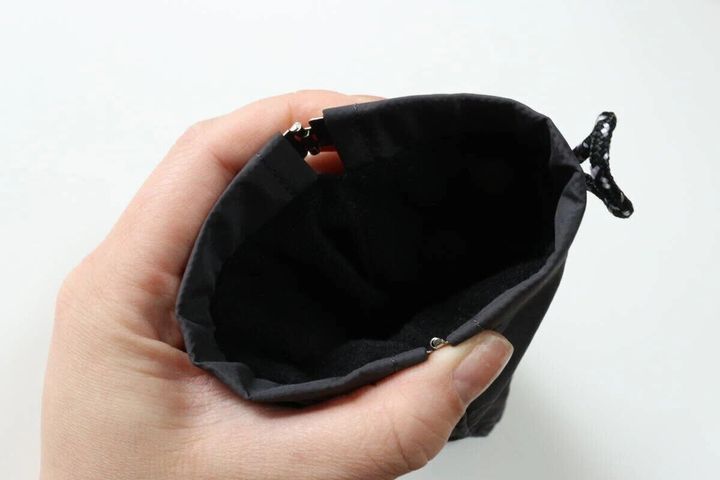 手で開かれたグレーのバネ口ポーチの開口部