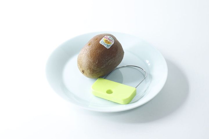 白い皿にキウイと緑色の皮むき器が置かれている