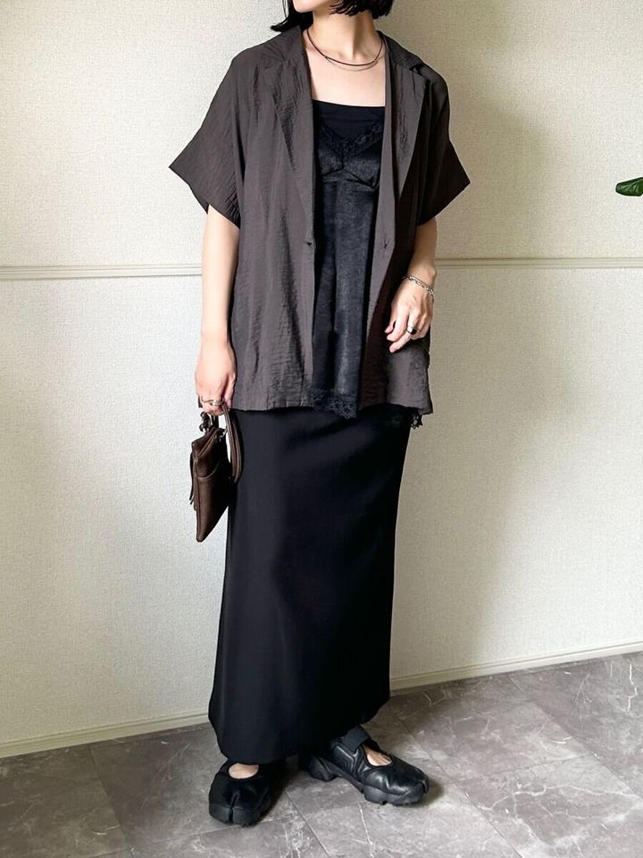 黒いロングスカートに黒いサテンキャミソールと茶色の半袖ジャケットを重ね着した女性の全身