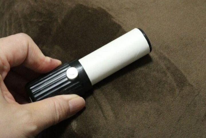 右手が白いロール部分が見える粘着クリーナーを茶色い布の上で持っている