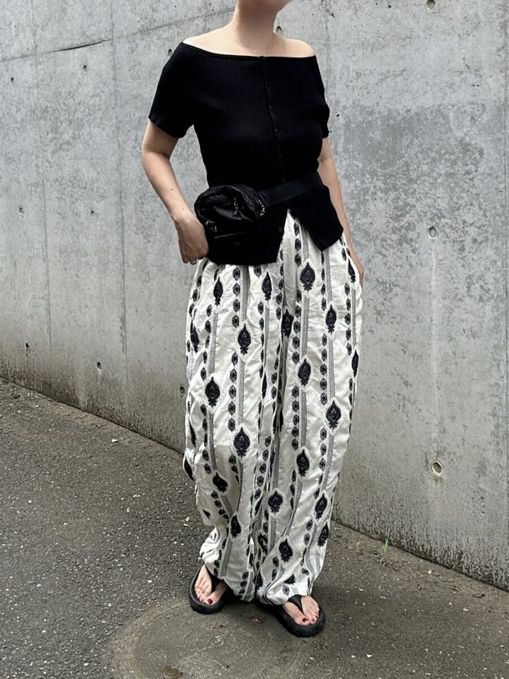 黒オフショルと大柄刺繍パンツの女性。ウエストポーチを着用し屋外に立つ。