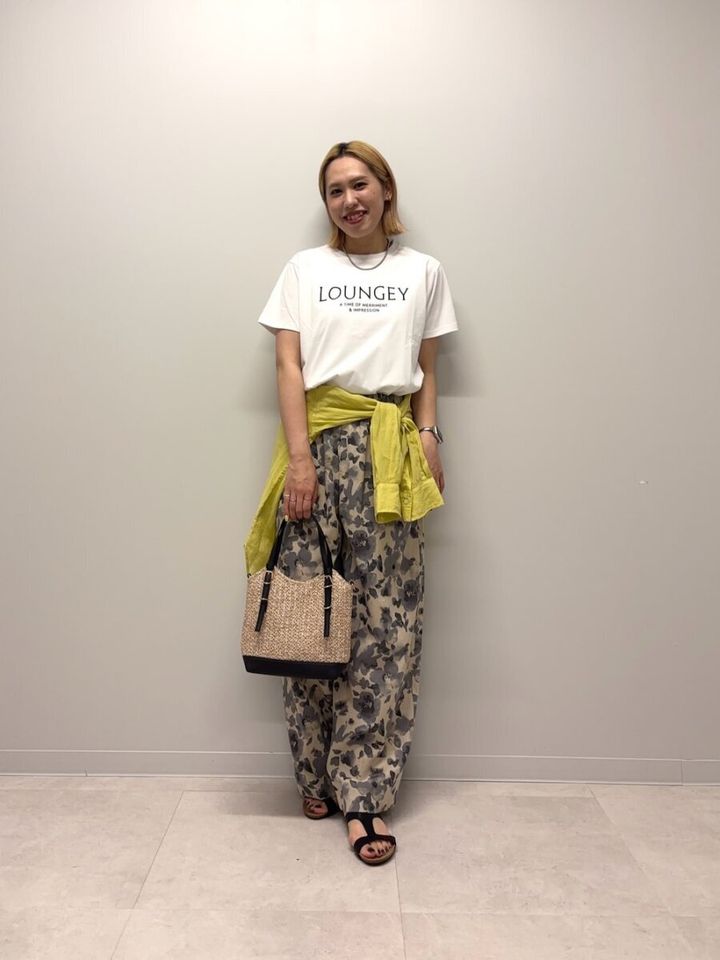 白ロゴTと迷彩柄パンツの女性。腰に黄色のシャツを巻き、かごバッグを持つ。