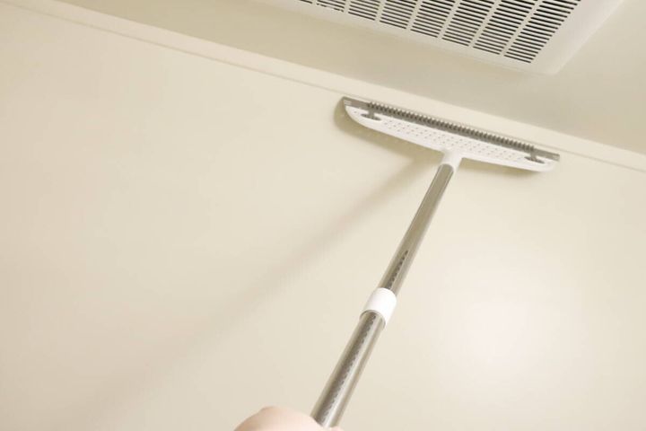 ワイパーほうきで壁の高い場所を掃除している様子。