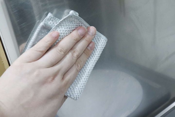 手が「凄腕くんお助けクロス」のマイクロファイバー面でステンレス壁面を拭いている