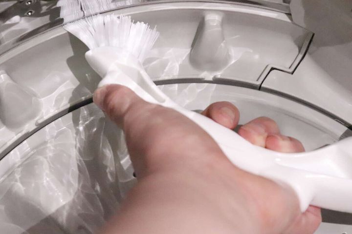 洗濯槽の縁の溝をスリムな白いブラシで掃除している手元