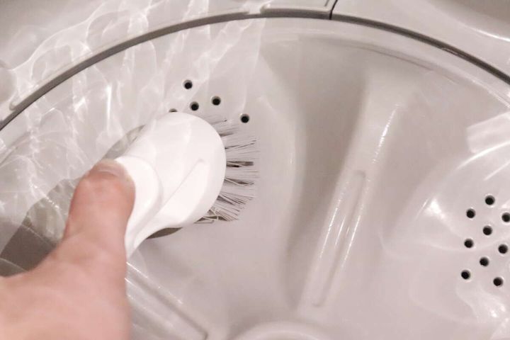 洗濯槽の底面を丸いグレーのブラシで掃除している手元