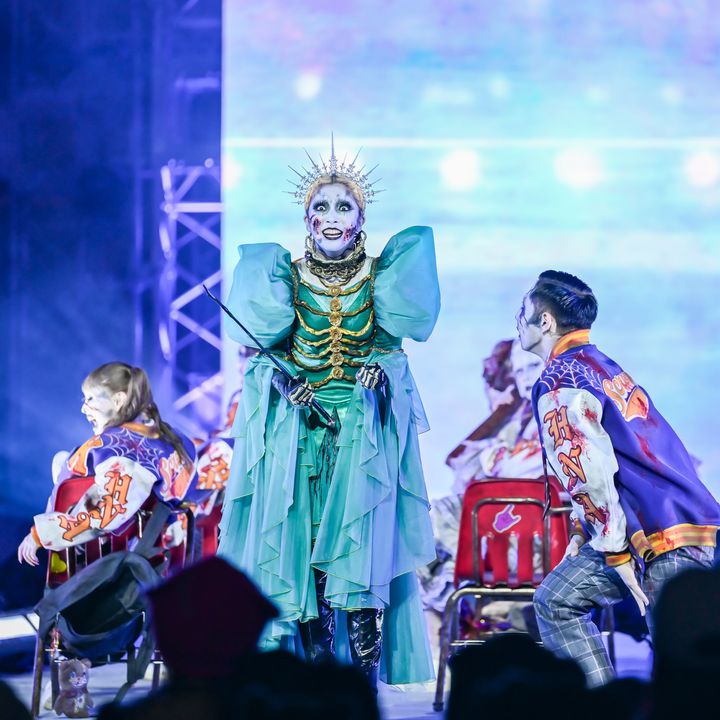 青緑色のドレス風衣装でステージ中央に立つ出演者