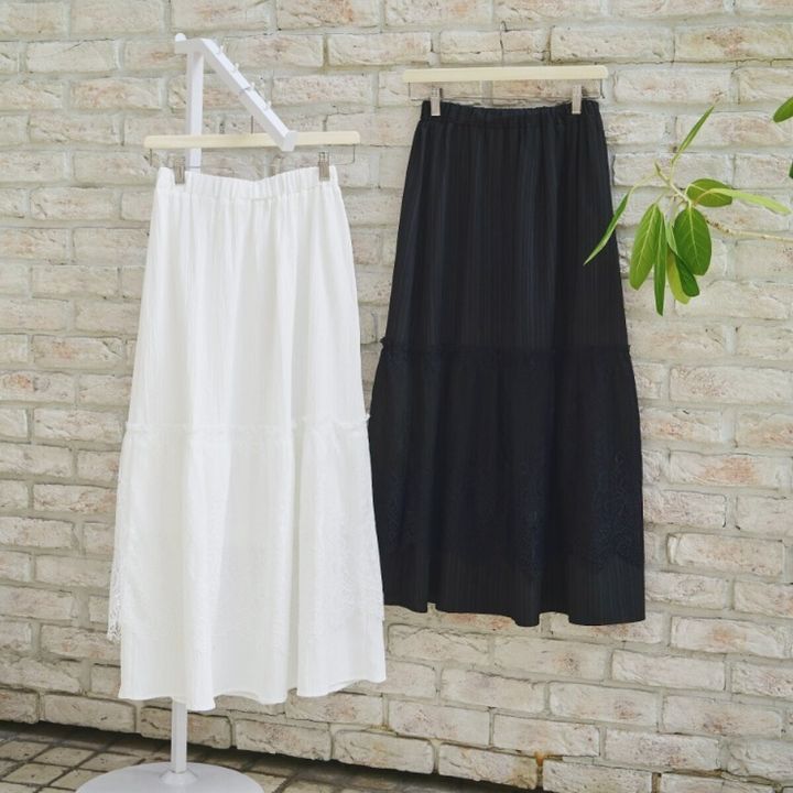白と黒のレーススカートがハンガーにかけられレンガ壁を背景に並んでいる。