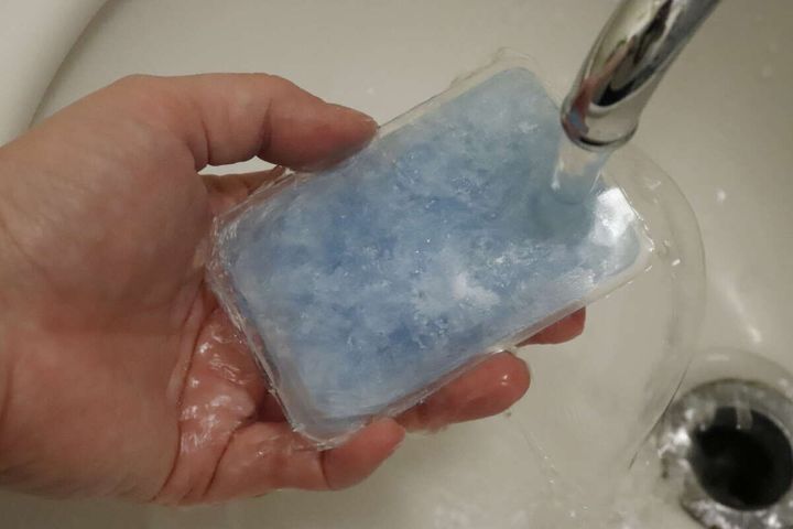 手に持ったスマホ冷却パッドを蛇口から出る水で洗っている様子