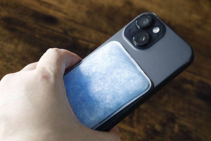 スマートフォンの背面に青い冷却パッドを貼り付けている様子