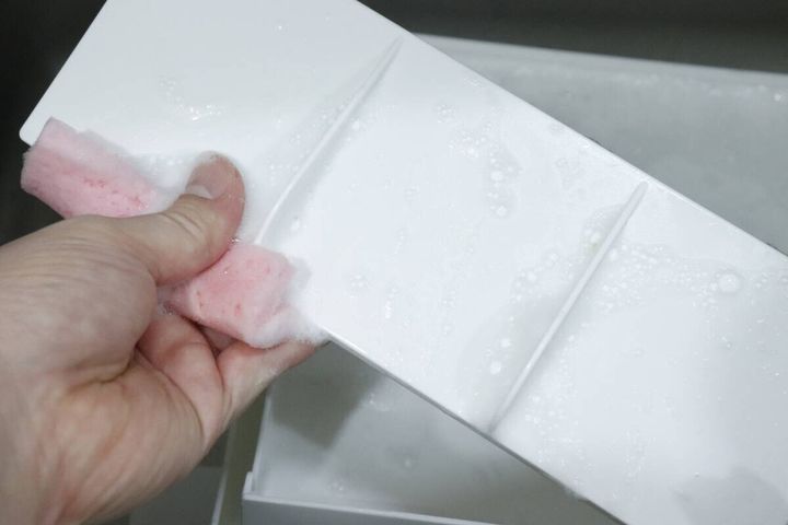 ピンクのスポンジでケースの仕切りを洗う手元