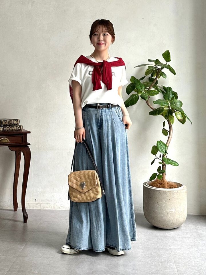 白ロゴTシャツとワイドデニム、赤いカーディガンを肩掛けした女性