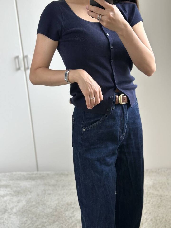 ネイビーのカーディガンとワイドデニムを着用した女性がスマホを構える