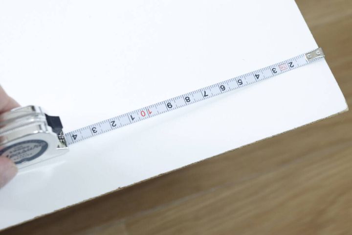 キーホルダーメジャーで白い板の長さを測っている手元のアップ