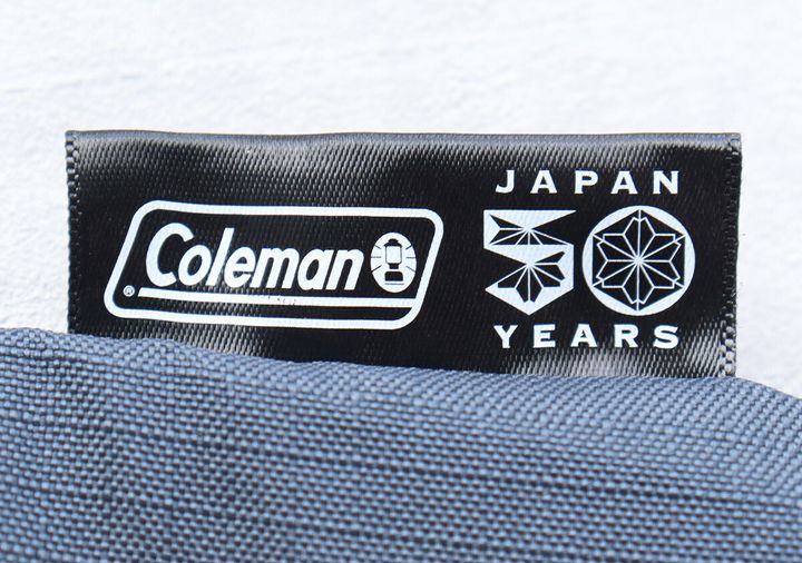 トートバッグに縫い付けられた「Coleman JAPAN 50 YEARS」の黒いタグのクローズアップ。
