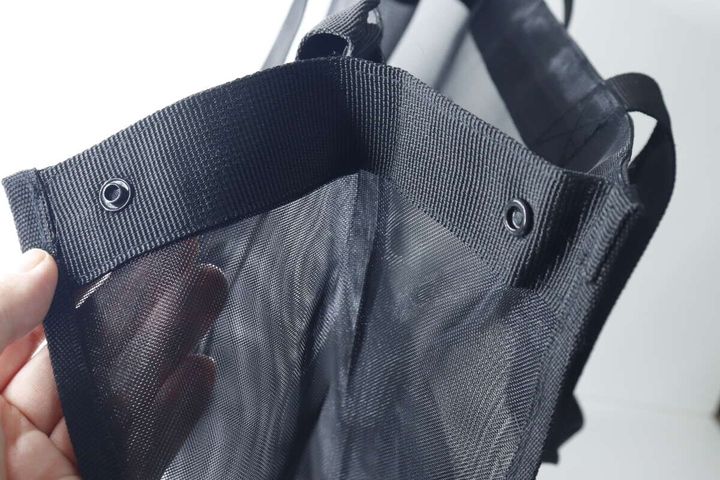 バッグのサイドにあるボタンを指で示している手元
