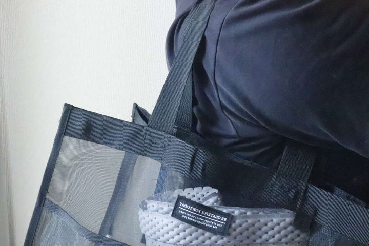 黒いメッシュバッグを肩に掛けている人の上半身、バッグの中身が少し見える