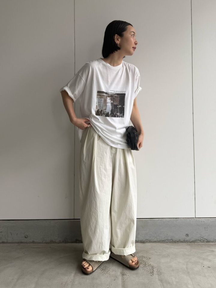 フォト白Tにオフ白ワイドパンツ、黒いミニバッグを持つ女性