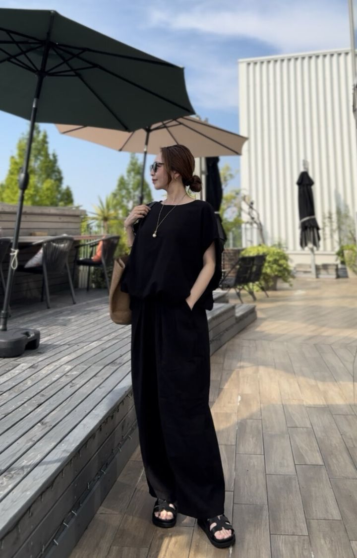 黒いリネンセットアップの女性が屋外テラスで横向きに立つ