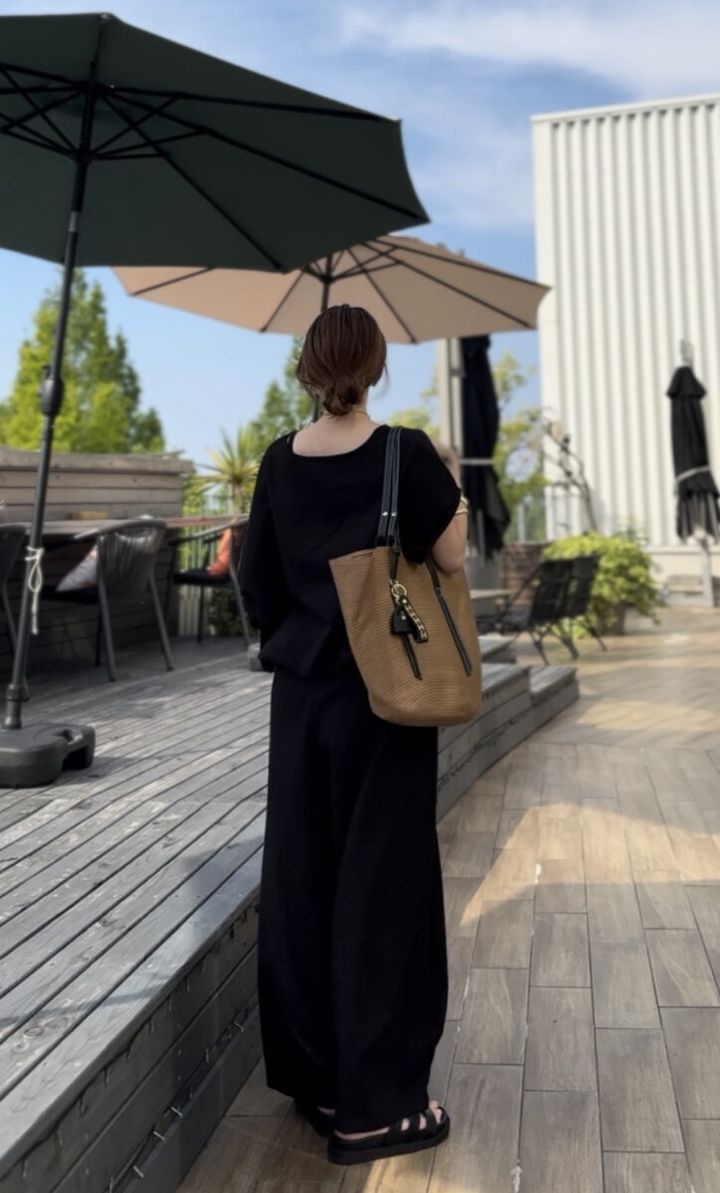 黒いリネンセットアップの女性が屋外テラスで後ろ向きに立つ