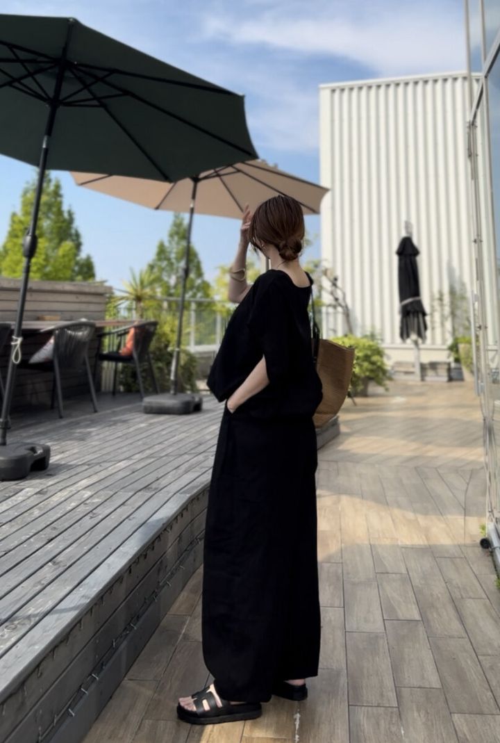 黒いリネンセットアップの女性が屋外テラスで横向きに立つ