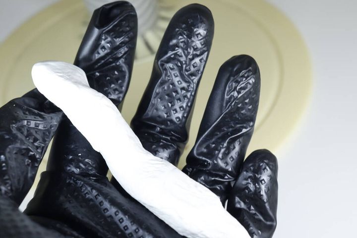 黒いゴム手袋をはめた手のひらに細長く練られた白いすきまパテ