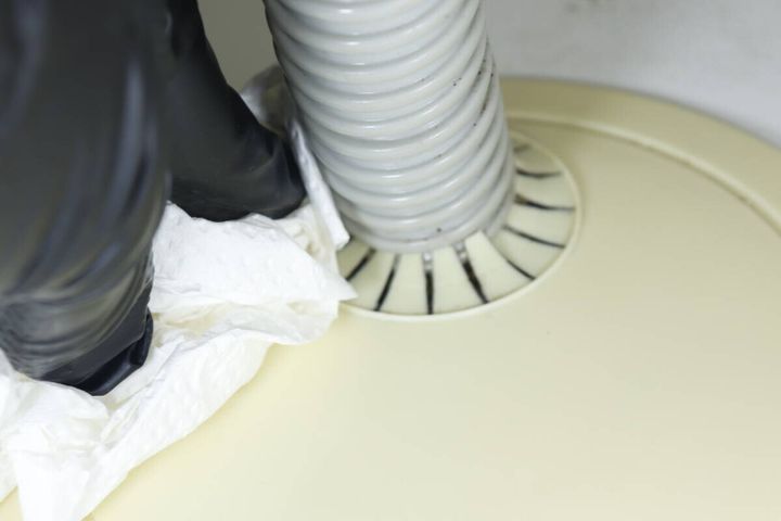 洗濯機の排水ホースと床の隙間を白いペーパータオルで拭き掃除している