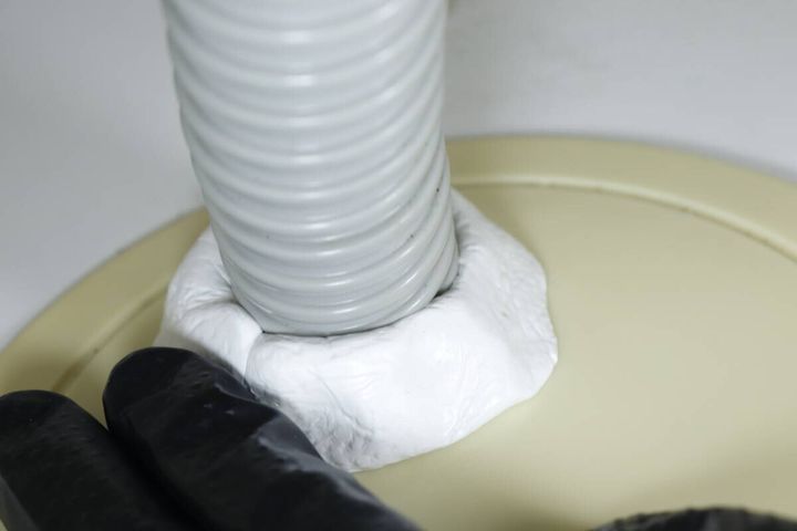 洗濯機の排水ホースと床の隙間に白いすきまパテを充填している様子