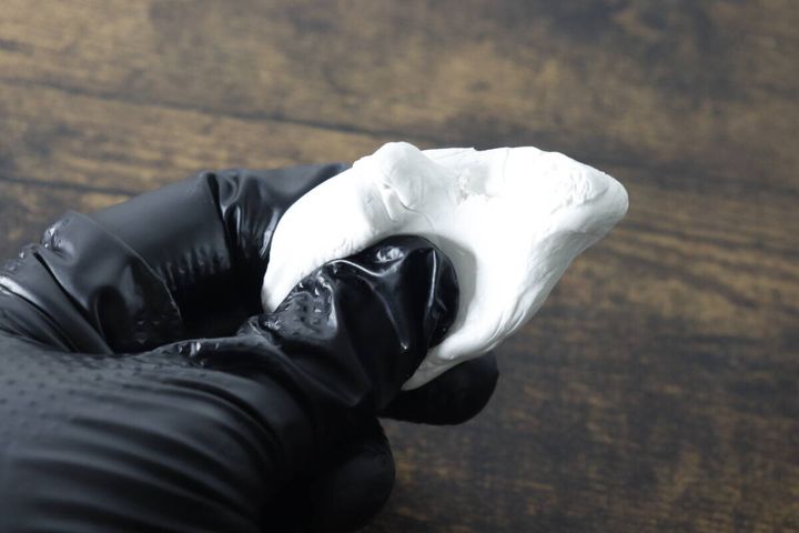 黒いゴム手袋をはめた手で白いすきまパテを練っている様子