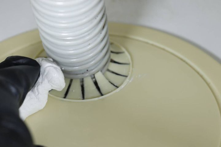 洗濯機の排水ホースと床の隙間に充填したすきまパテをならして整えている