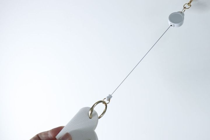 手が白いキーカバーを持ち、リールが伸びて鍵を操作する様子