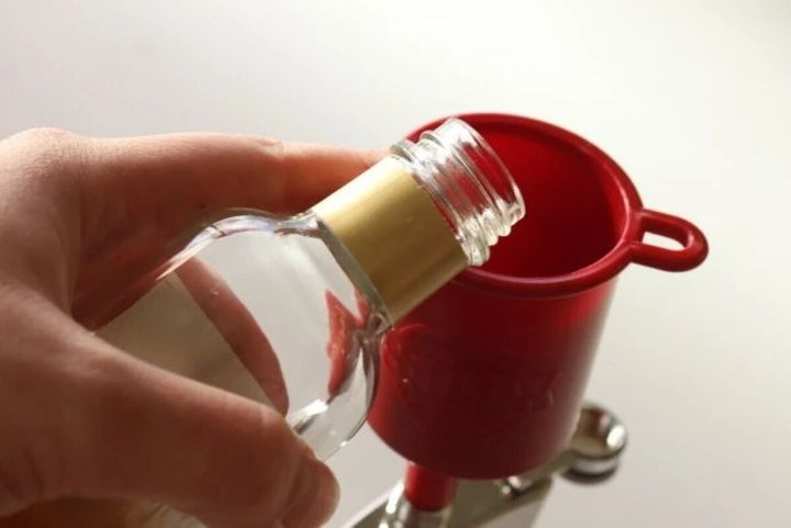 手が透明なボトルから赤いロートに液体を注ぎ入れている様子