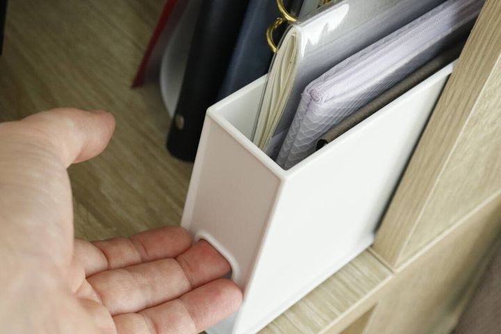 棚に置かれた収納ボックスから手帳を取り出す女性の手
